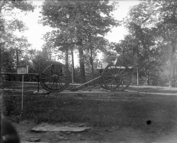 A cannon at Soldiers Home adorned with American flags near a sign reading "Keep off the grass."