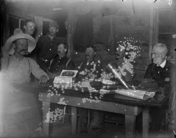 Men sitting around a table in a cabin at the Leighton-Wyoming mining camp. A box of cigars and a phonograph record player are sitting on the table. D.S. Crandall is most likely the white-haired gentleman on the far right.