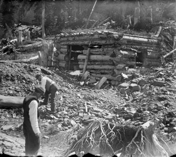 Men from the Leighton-Wyoming mining operation clearing the area directly around a log cabin that is either in the process of being built or being destroyed.