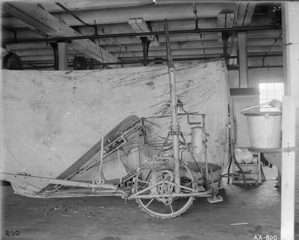 Corn binder, possibly a prototype or experimental model, displayed in front of a dirty canvas sheet in a factory setting, possibly at the McCormick Reaper Works in Chicago.