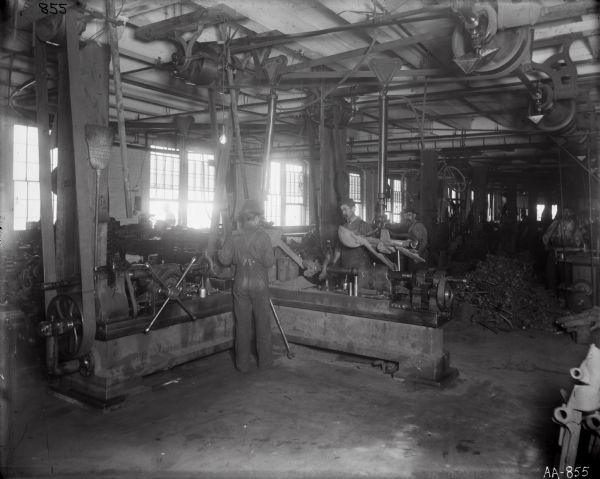 Factory workers amid heavy machinery, most likely at the McCormick Reaper Works. A bicycle is hanging from the ceiling in the background.