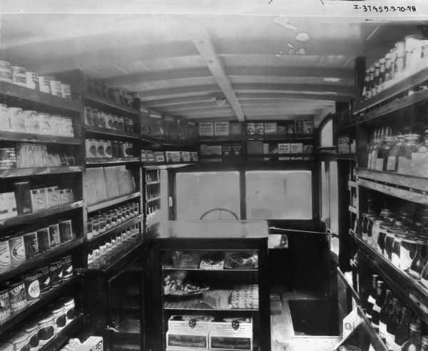 An interior view of "Hook's Rolling Stores" International fleet truck. The mobile grocery store appears to include dry goods, including Kellogg's Corn Flakes and Pep cereals, canned goods, bottles and cans of beverages, and a small selection of refrigerated goods.