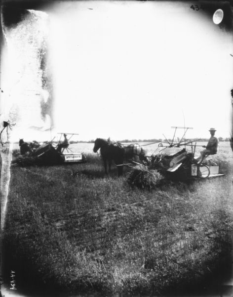 Two Men Using Horse-Drawn Binders in a Field Two men are using horse-drawn McCormick binders in a field. One of the horses is wearing a fly-net.