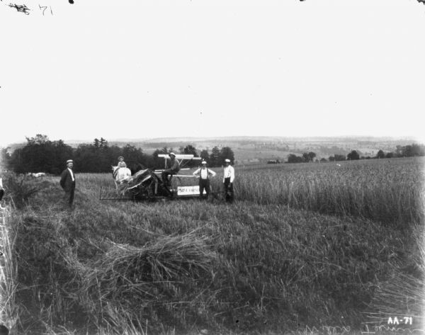 Man and Boys Posing with Horse-Drawn Binder Three men are standing near a man sitting on a horse-drawn McCormick binder. A young boy is sitting backwards on the horse pulling the binder. Another horse is in the background on the left.