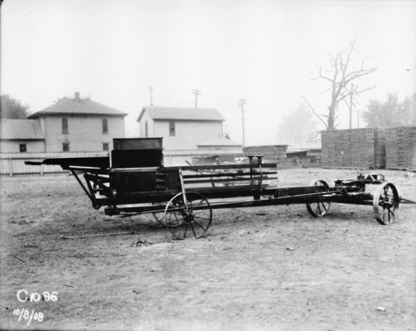 Hay Press Hay press in a yard with stacks of wood or pallets. In the background are buildings behind a fence.