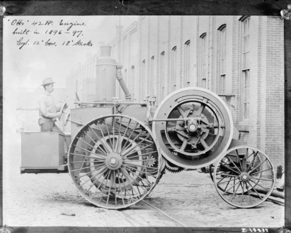 Man Driving Otto Tractor near Factory Building Right side view of man driving a tractor outdoors near a brick factory building. Caption on photograph reads: "Otto 42 H.P. built in 1896-1897. Cyl. 12" bore, 18" Stroke."