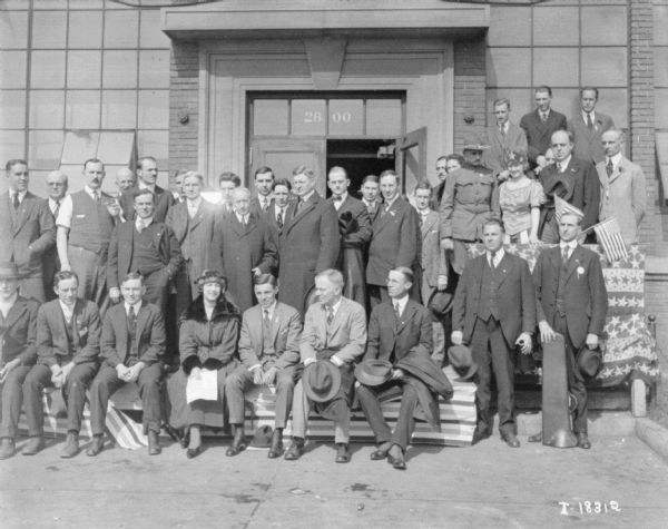 Outdoor Group Portrait of Men and Women Group portrait of men and women posing outdoors with American Flags and bunting in front of the entrance to a building.