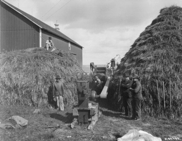 Threshing Operation Men are posing with two large stacks of hay at a threshing operation.
