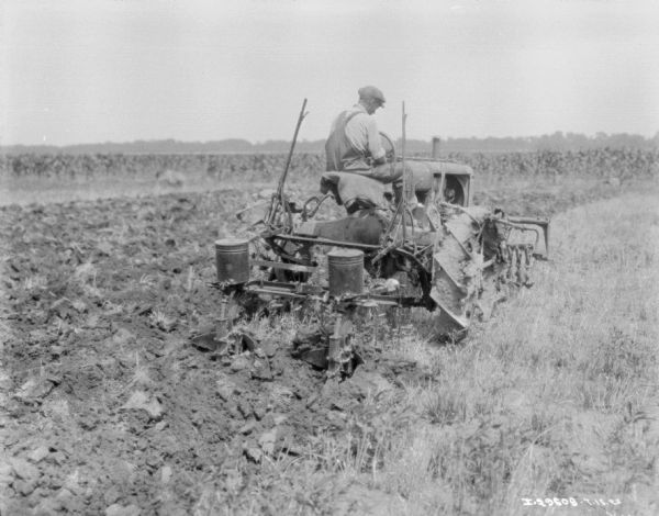 Man with Farmall Tractor Planting Field Three-quarter view from right rear of a man using a Farmall tractor to plant in a field.