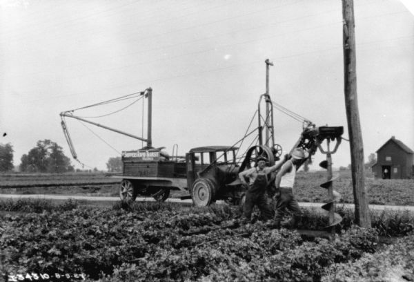 Truck and Telephone Pole Installation Two men are using a large auger to dig a hole for installing telephone poles. A truck is parked nearby, used for installing the poles. The sign on the side of the truck reads: "Shippers Rapid Transit, Toledo, O."