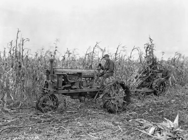 Farmall-Drawn Corn Pickers A man is driving a Farmall tractor in a cornfield, pulling another man sitting on a corn picker.