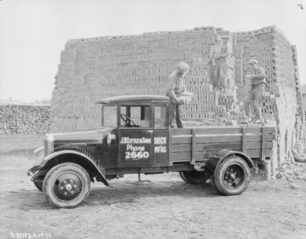 Loading Bricks on Delivery Truck Three men are loading a delivery truck with bricks. They are working in a yard, and one of the men is standing on a large stack of bricks in the background. The sign on the truck reads: "J.B. Little & Sons, Brick Mf'gs."