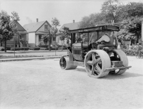 Cement Roller Three-quarter view from left rear of a man driving a cement roller. A group of people are watching in the background on the right. The sign painted on the front of the tractor reads: "Cicero Vehicle Tax Dept."