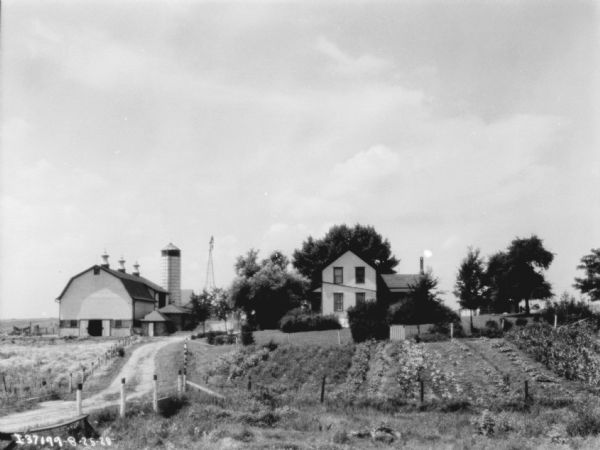 Farm Buildings View across field and garden towards a farmhouse and farm buildings. There is a road on the left.