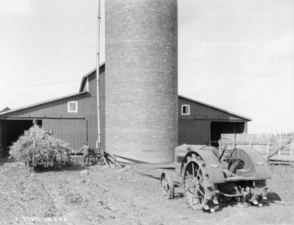 Tractor Powered Ensilage Cutters View towards men working with a tractor powers ensilage cutter to fill a silo.