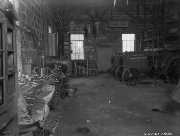 View of the interior of a repair shop. Tractors are parked in the background on the right.