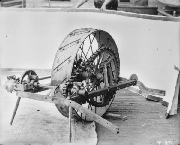 Wheels and Chain Drive Mechanism Close-up of a wheel and a chain drive mechanism. There is a man (face out of frame) standing behind a light-colored backdrop in the background.