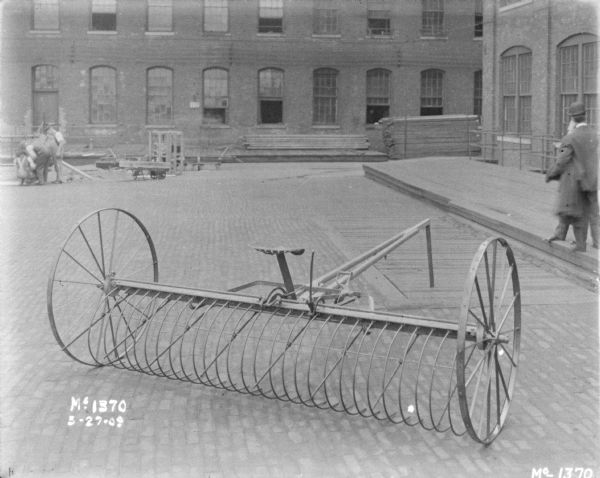 Dump Rake Outdoors in Yard at McCormick Works Dump rake, with men chatting in yard on the right. Other men are working in the background on the left near a brick factory building.