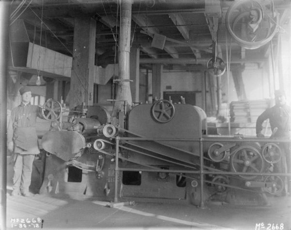 Two men are standing indoors next to a manufacturing machine at McCormick Works.