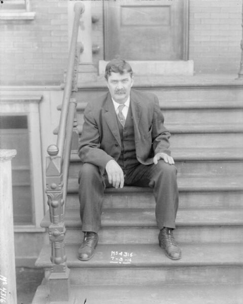 Man Sitting on Steps Portrait of a man wearing a suit sitting on the steps of a stoop to a brick building.