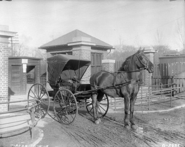 Man Driving Horse-Drawn Buggy Leaving Plant A man is driving a horse-drawn buggy out through the gates of a plant.