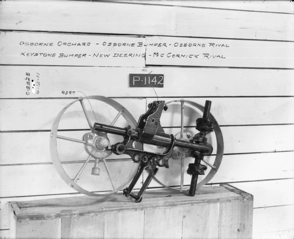 Osborne Disk Harrow Parts Parts are set up on a box in front of a wall with writing that reads: "Osborne Orchard — Osborne Bumper — Osborne Rival, Keystone Bumper — New Deering — McCormick Rival." Includes part numbers: P-1142, 9397.