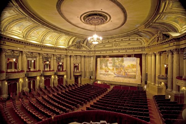 View of Al. Ringling Theatre's auditorium and stage from a rear box.  View includes a painted theater curtain and shows the auditorium's state before restoration plans have been completed.