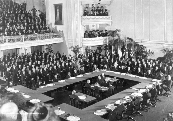 A general view of the Disarmament Conference in Memorial Continental Hall from the balcony. Politicians sit around tables, and an audience gathers on the main floor and balconies. Photograph published by Underwood and Underwood.