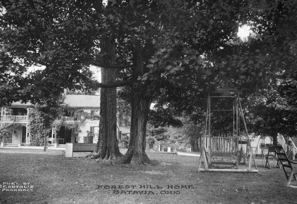 Front view of Forest Hill Home. Decorative railings and columns are shown on the country home, and two trees lie in the foreground with a swing, chairs, and tables. Caption reads: "Forest Hill Home, Batavia, Ohio."