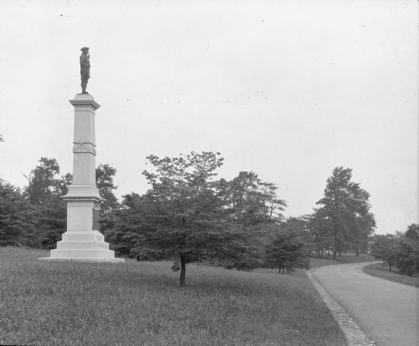 Side view of the New Jersey Brigade Monument. Atop the monument stands a New Jersey Continental Soldier, and the base reads, "New Jersey Brigade," and "Continental Army." In front of the monument, Inner Line Drive curves to the right.