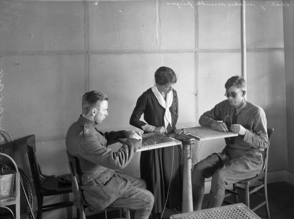 Interior of the United States General Hospital No. 7, as designated by the surgeon-general in 1918. Intended for returning soldiers' physical reconstruction, Roland Park's facility specialized in the treatment of the blind and deaf. A women teaches two blind men to weave cane seating.
