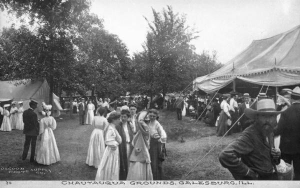 View of the Chautauqua Grounds, founded in 1874. Groups of people gather around tents on the grounds. Caption reads: "Chautauqua Grounds, Galesburg, ILL."