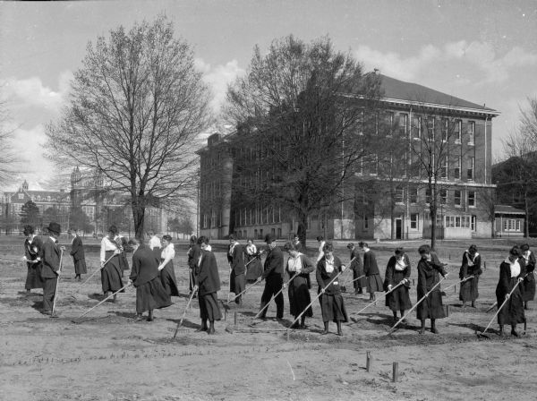 View of students gardening at Winthrop College, founded in 1886. School buildings stand in the background.