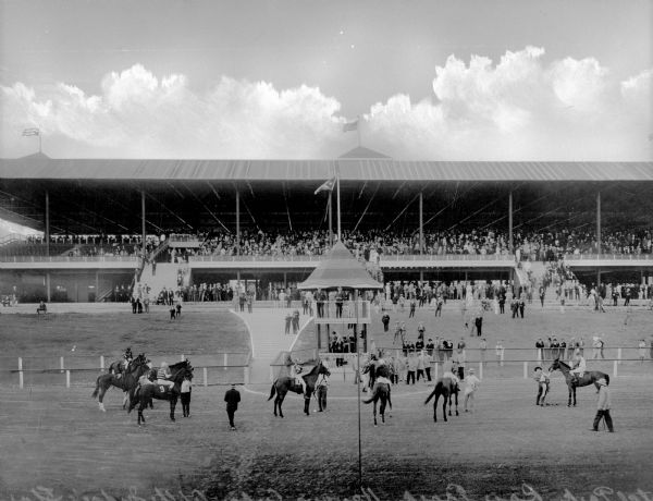 Horses stand near a judge's booth at Oriental Park Racetrack while spectators watch from a grandstand in the background. The racetrack was founded in 1915 in Havana, Cuba.