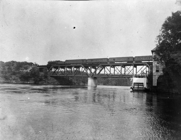 View along right side of shoreline toward a Chicago, Minneapolis, and St. Paul train crossing a bridge over the Wisconsin River.