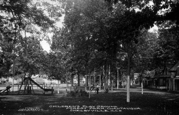 Children play in Forest Park at the Chautauqua Grounds, an institution founded in 1874. Residences can be seen beyond the playground at right. Caption reads: "Children's Play Ground, Forest Park, Chautauqua, Shelbyville, ILLS.