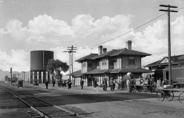 Exterior view of Maricopa Train Depot. Men gather near the railroad tracks.