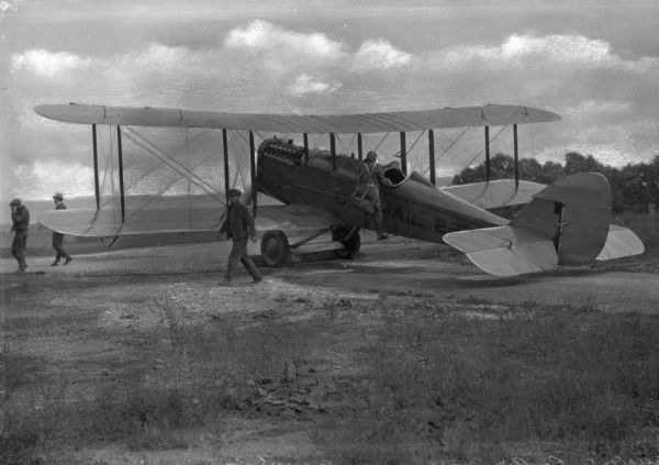 View toward an air mail pilot climbing into his airplane to get ready to leave the field. Other men are walking away from the airplane.