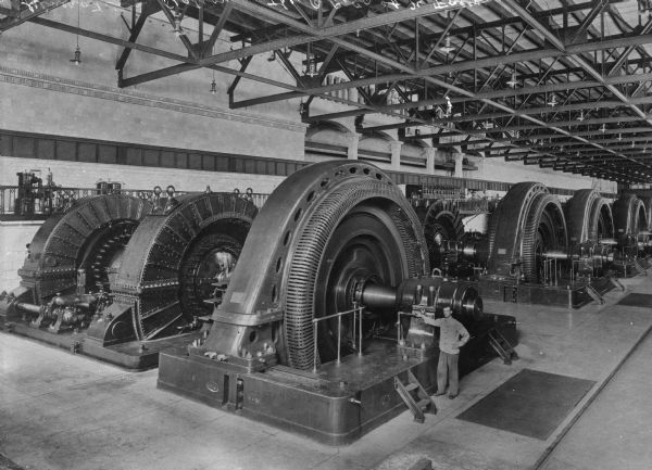 Elevated view of the interior of a generator plant. A man is standing next to the machines.