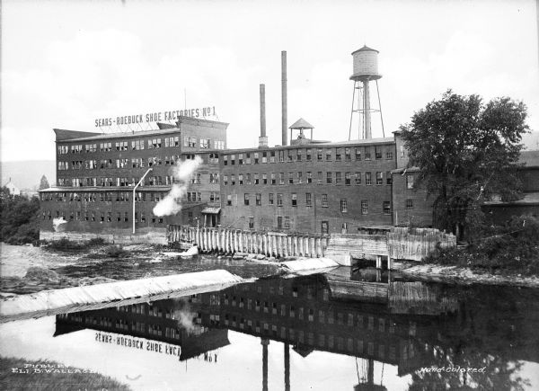 View across water toward the Sears and Roebuck Shoe Factory No. 1. The factory is reflected in the water.