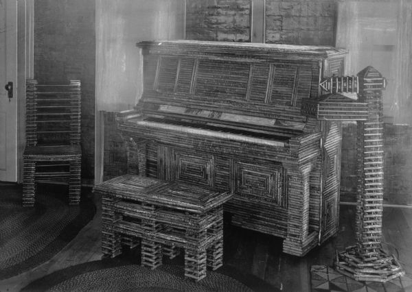 Interior view of the Paper House, featuring a piano, a bench, a lamp and a chair constructed with rolls of paper.