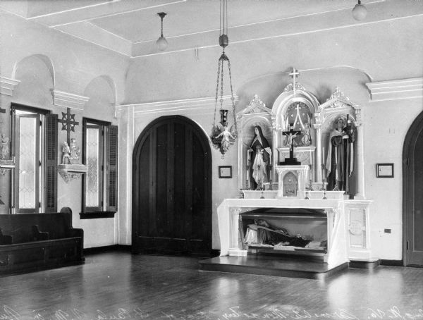 A view of the altar with the body of St. Paula beneath. Two statues flank the  crucifix.  A row of pews is on the left.