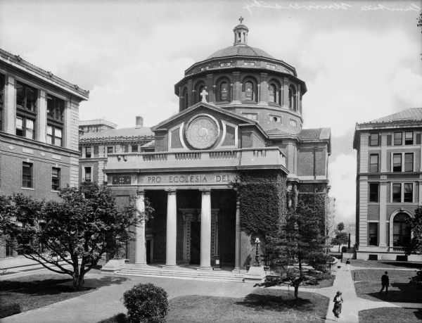 Slightly elevated view of St. Paul's Chapel and the surrounding buildings. The structure features a Classical-style porch, columns, pediment, and dome. Arched, stained glass windows line the dome, and on top is a bell tower with crucifix.