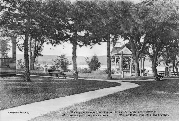 View across lawn toward a gazebo, section of a porch, and benches on the campus of St. Mary Academy. The lawn overlooks the Iowa Bluffs across the Mississippi River. Caption reads: "Mississippi River and Iowa Bluffs, St. Mary Academy. Prairie du Chien, Wis."