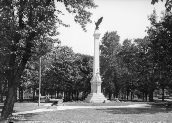 View of the monument to Civil War soldiers, located in what is now called the Watertown Veterans Memorial Park. A large eagle tops the monument. Above the base is a soldier standing with his gun. Caption reads: "Lewis Memorial, Monument City Park, Watertown, Wis."