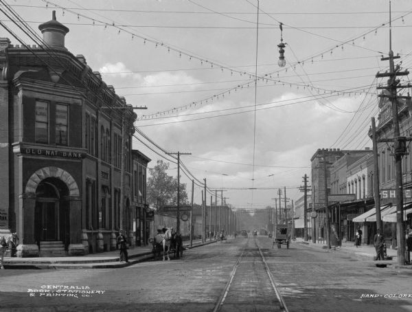 View of the Broadway Street business district, with electric lights and power lines overhead, and streetcar tracks. Text on bank building (far left) reads: "Old Nat Bank 1888." Sign in upper windows reads: "Albert B. Rodenberg Law Offices."