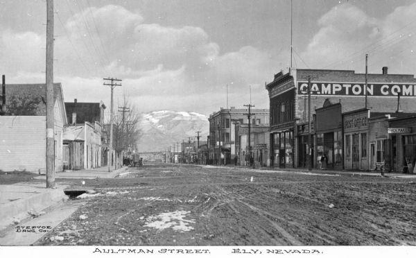 View of Aultman Street, the main thoroughfare. Mountains are in background. Business signs read: "Shoemaker," "Ely Post Office," "Campton Commercial Co.," "Olympia Fruit Store," "Veteran" and "Vienna Cafe." Caption reads: "Aultman Street. Ely, Nevada."
