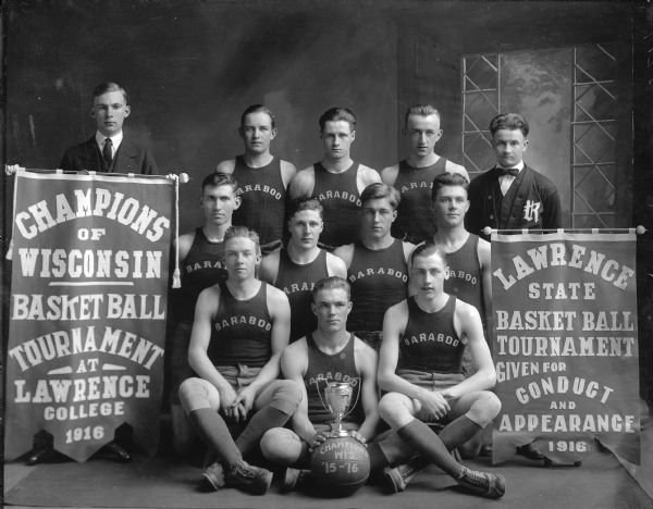 A group portrait in front of a painted backdrop of the 1916 Baraboo basketball team, winners of the Wisconsin State Basketball Tournament held at Lawrence College. Banners identify the team as the champions, and cite the team for "Conduct and Appearance."