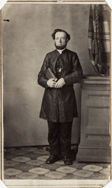 Full-length carte-de-visite portrait of George W. Honey, F & S, 4th Wisconsin Cavalry, standing, wearing clergy dress and holding a bible.