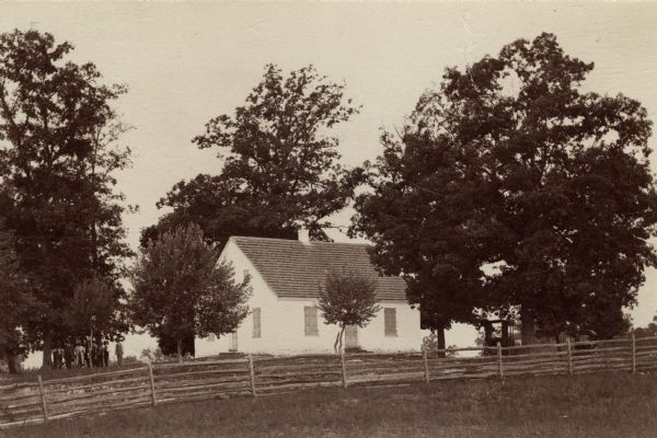 Site of the Battle to Antietam, The Dunker Church. A group of men stand among trees on the left. Horse-drawn carriages are under trees on the right.